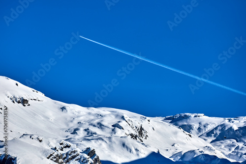 Verschneite Berge und ein Flugzeug am Himmel