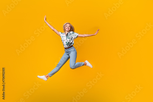 Full size photo of positive girl dressed print shirt stylish jeans flying hold palms like wings isolated on yellow color background
