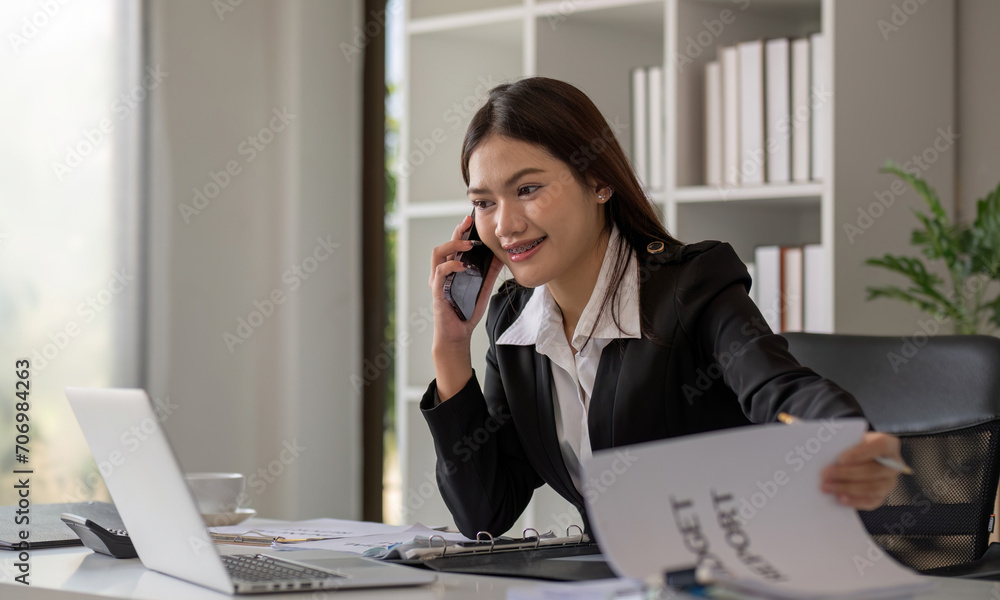 Cheerful Asian businesswoman talking on the phone working in modern office Happy Asian businesswoman company manager wearing a suit is talking on the phone sitting in the office. Cheerful Asian businesswoman talking on the phone working in modern office Happy Asian businesswoman company manager wearing a suit is talking on the phone sitting in the office.
