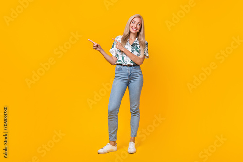 Full size photo of cute gorgeous girl dressed print shirt jeans look directing at offer empty space isolated on yellow color background