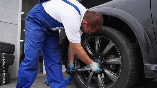 Auto mechanic secures car wheel with torque wrench for precision. Worker in uniform installs tire ensuring safety, reliability in automotive repair shop scenario. Professional car maintenance task. photo