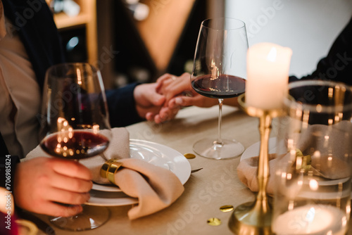 Romantic date by candlelight at night. Proposal hand and heart. Hands man and woman hold glasses at home. Toast. Couple in love drinking wine. Cheers. Dinner setup table for couple on Valentine s day.