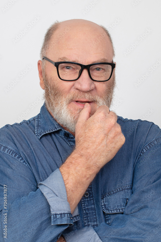 Portrait of an attractive gray-haired man with glasses wearing a denim shirt isolated on a gray background. Portrait of an attractive gray-haired man with glasses wearing a denim shirt isolated on a gray background.