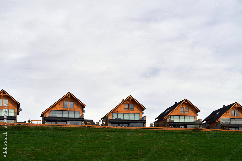 Cozy wooden homes with balconies and windows that offer a panoramic view of the green landscape and the cloudy sky. Cozy wooden homes with balconies and windows that offer a panoramic view of the green landscape and the cloudy sky.
