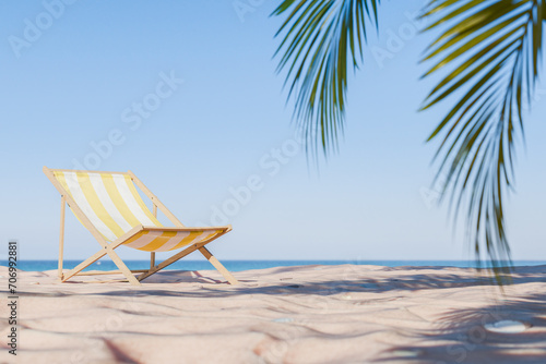 3D rendering of a striped beach chair on sand with palm leaves overhead, summer relaxation concept.