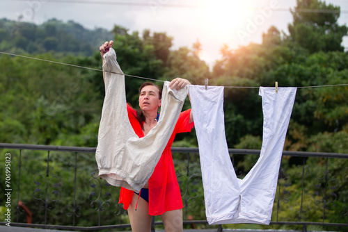 A woman hangs her washed clothes to dry outdoors.