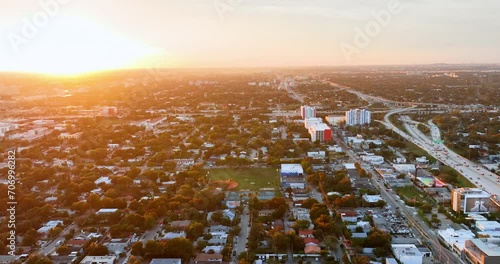 Evening panorama of the city of Miami with small houses, trees and streets with cars. Road interchange. Bright yellow sun on the horizon. photo