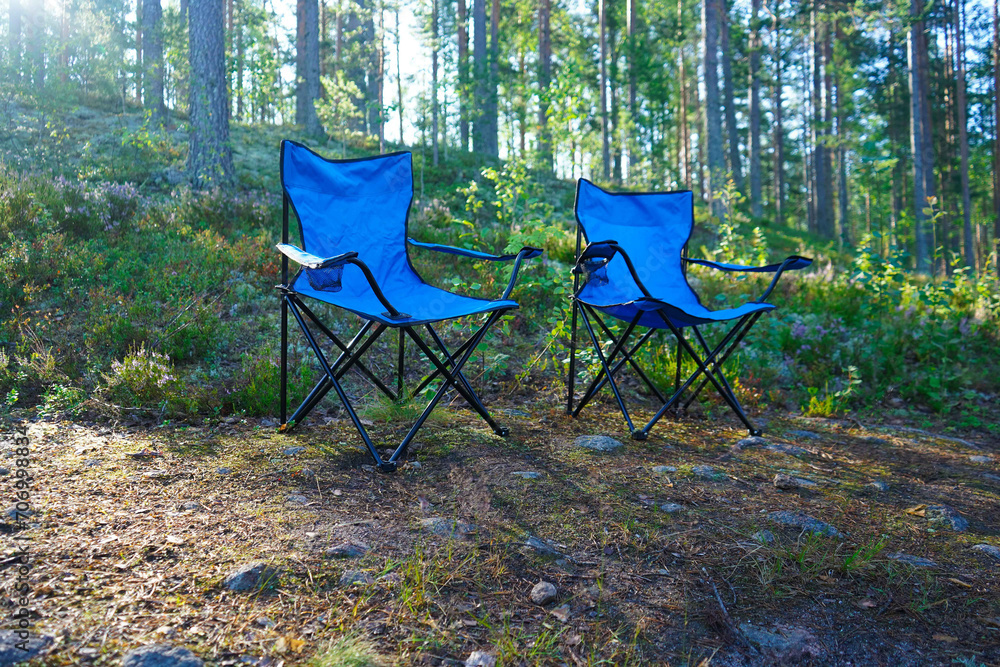 Two empty blue chairs for Camping folding garden chairs on the wild pine forest on a sunny day. Two empty blue chairs for Camping folding garden chairs on the wild pine forest on a sunny day.