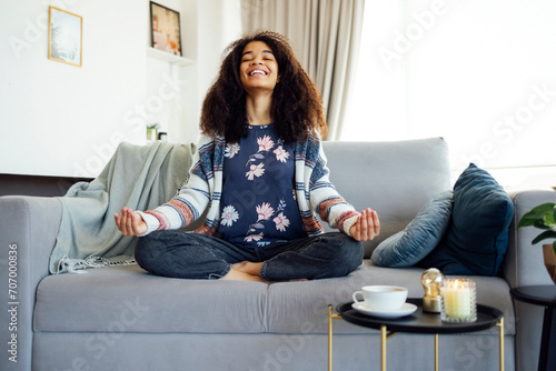 Cute smiling afro american woman is learing yoga at home sitting on the sofa photo