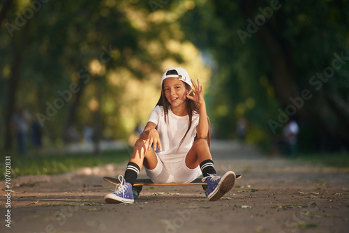 Chilling, sitting and relaxing. Happy little girl with skateboard outdoors