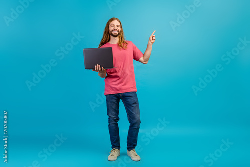 Full body photo of attractive guy hold laptop indicate finger empty space ad offer isolated on blue color background