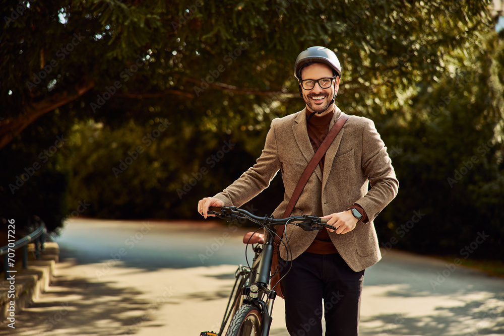 Portrait of a businessman in a suit pushing a bicycle through a park.