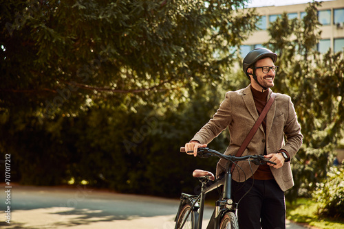 Fototapeta Naklejka Na Ścianę i Meble -  A smiling businessman with a helmet and glasses on pushing his bicycle and walking to work.
