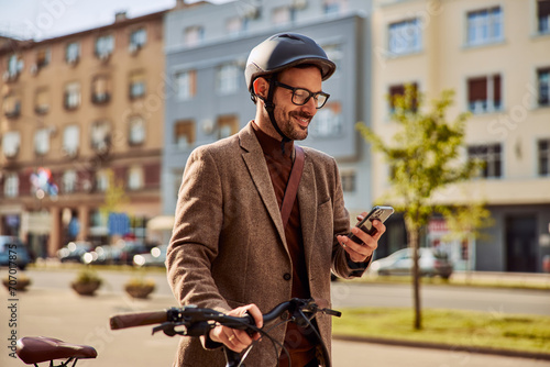 A smiling businessman using a mobile phone and pushing a bicycle while going to work. photo