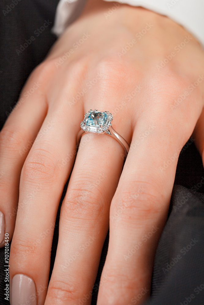 Beautiful female hand with gold ring with diamonds and emerald on gray background Beautiful female hand with gold ring with diamonds and emerald on gray background