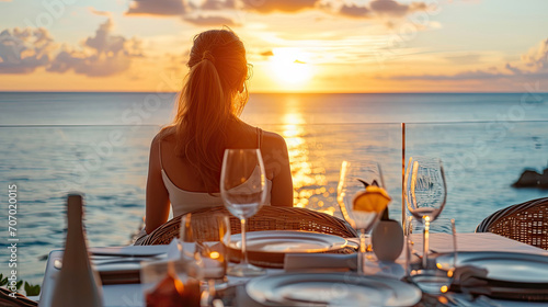 Romantic dinner on sunset. Woman sitting alone on table set with lantern for a romantic meal on beach, yachts and ocean on background. Dinner for a couple in love in luxury outdoor restaurant