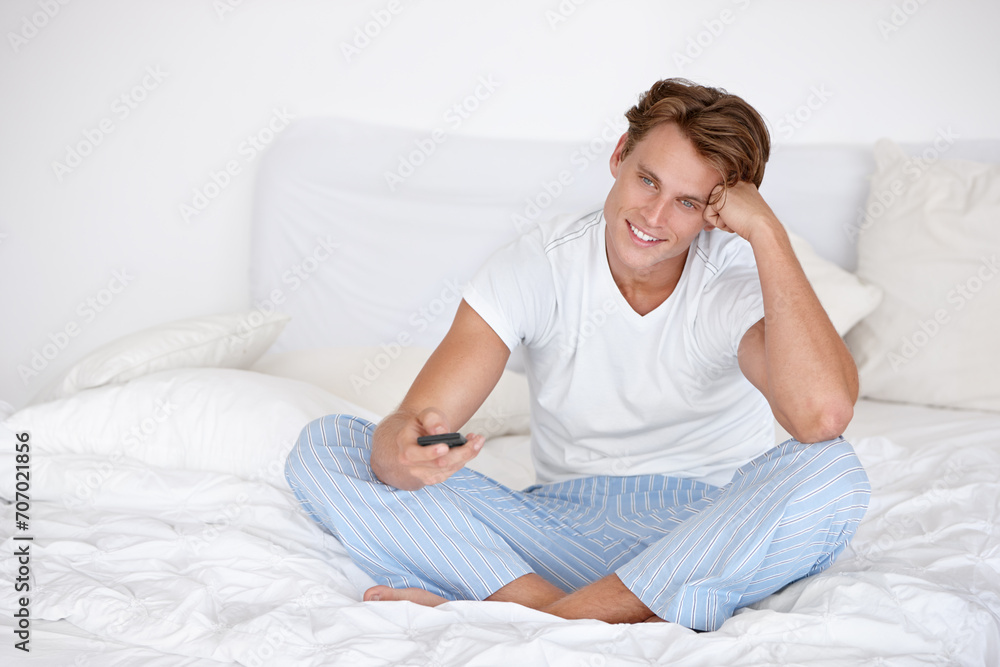 Happy man, morning and watching tv in bedroom with remote for streaming entertainment to relax. Smile, pyjamas or person enjoying television series, news or film with control for movie choice in home Happy man, morning and watching tv in bedroom with remote for streaming entertainment to relax. Smile, pyjamas or person enjoying television series, news or film with control for movie choice in home