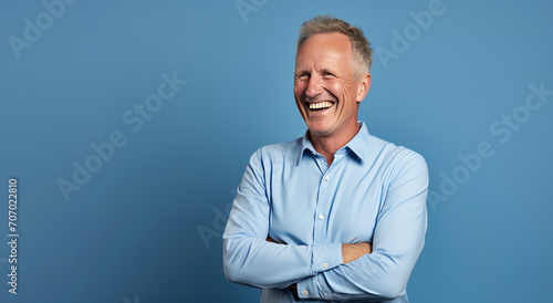Portrait of happy senior man laughing with arms crossed against blue background.