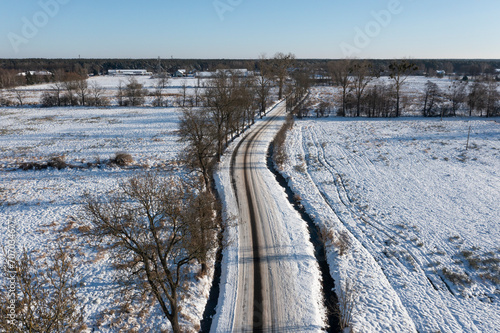 A road covered with snow among fields and meadows, view from a drone. © Kozioł Kamila