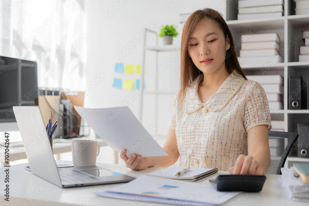 Working with finance and calculator in bank office, Asian female accountant working with laptop and financial documents in office