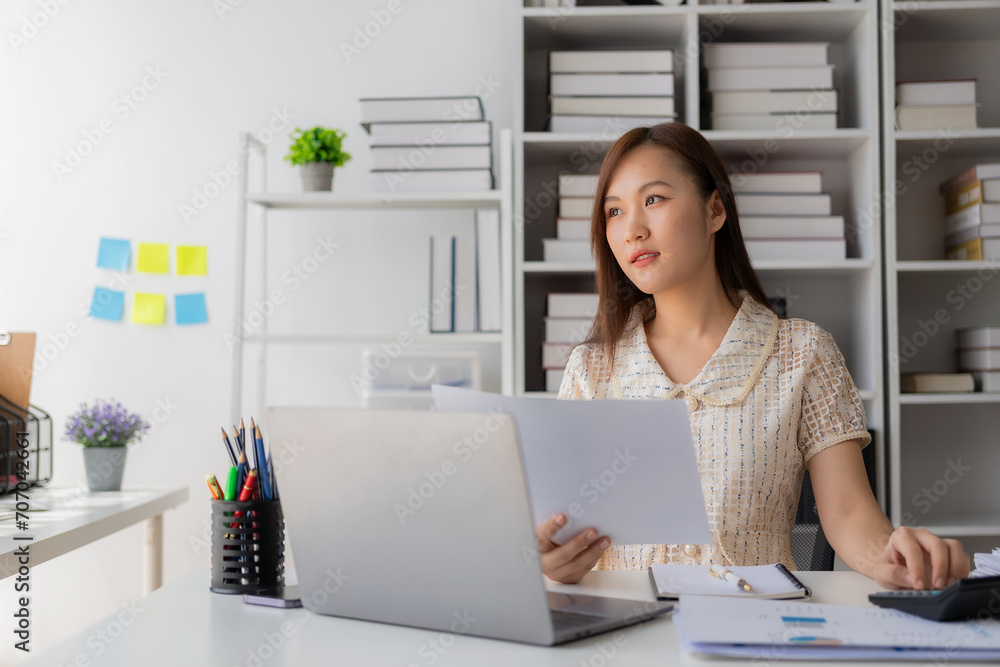 Working with finance and calculator in bank office, Asian female accountant working with laptop and financial documents in office Working with finance and calculator in bank office, Asian female accountant working with laptop and financial documents in office