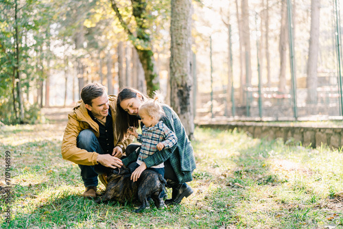 Little girl looks at mom and dad stroking a french bulldog in the forest