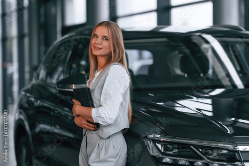 Leaning on the automobile. Woman in formal clothes is in the car dealership