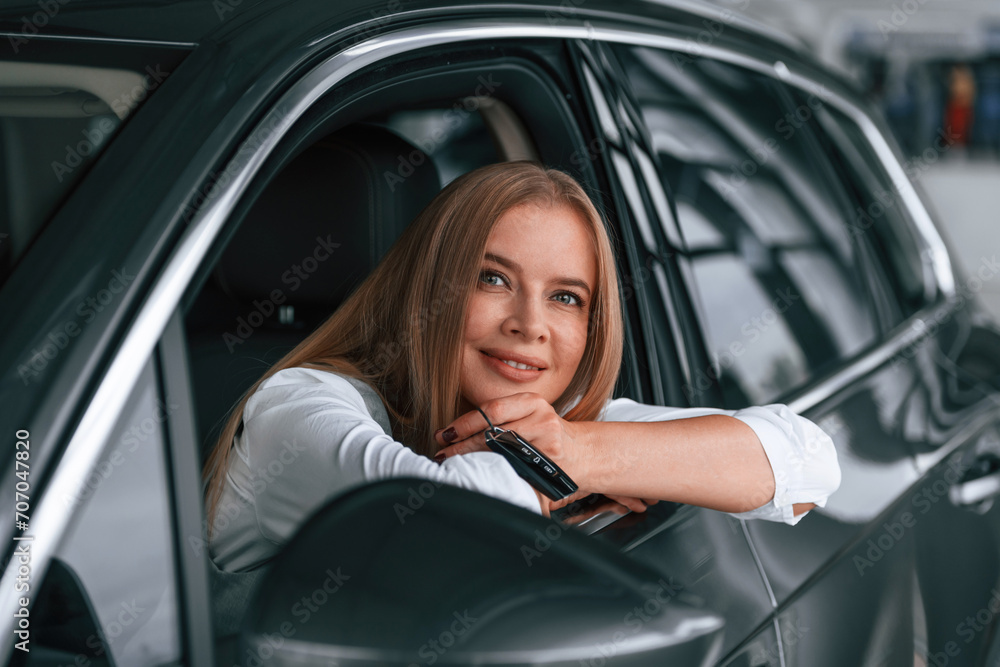 Looking from the opened window. Woman is sitting in a car and driving it Looking from the opened window. Woman is sitting in a car and driving it