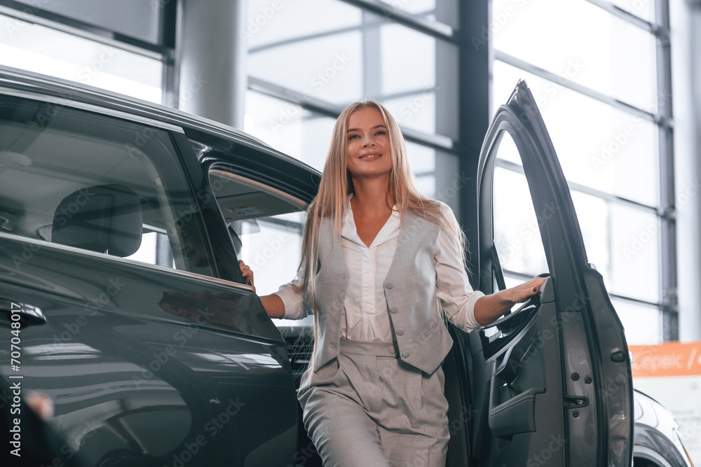 Woman is near the modern automobile in car dealership salon