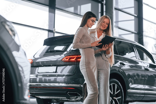 Standing and holding tablet. Female manager is helping woman customer in the car dealership salon © standret