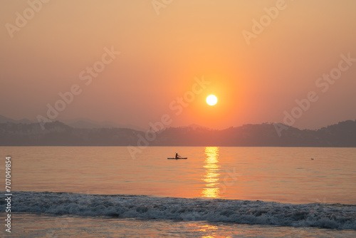 paddlesurf deporte practicado en el mar en el océano en la playa deporte extremo relajante rodeado de tranquilidad en un hermoso atardecer con la puesta del sol brillante y al horizonte montañas