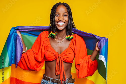 African american young smiling girl with braids, toothy smiles with pride rainbow flag at studio isolated over yellow background. Trans or bisexual concept.