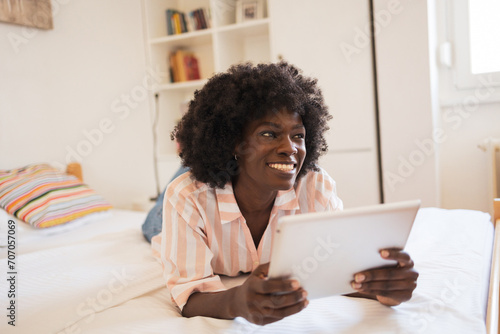 Thoughtful woman smiling while holding digital tablet in bed at home