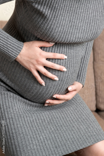 Pregnant Lady Having Massaging Lower belly Sitting On Sofa Indoor. Pregnancy Problems Concept. Maternity healthcare