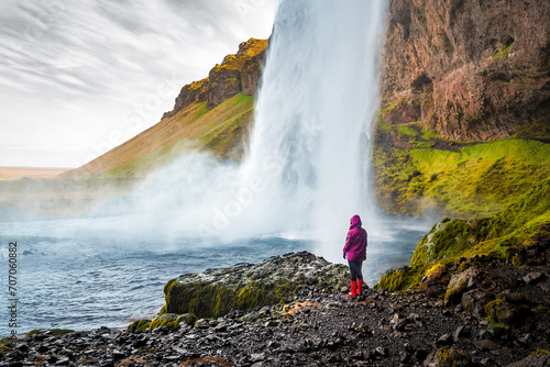 Tourist person in red raincoat watching Seljalandsfoss waterfall in Iceland photo