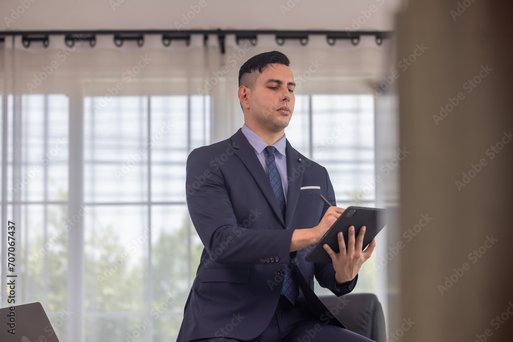 Male manager in suit multitask on laptop, tablet in modern office, talk to clients, analyze project Male manager in suit multitask on laptop, tablet in modern office, talk to clients, analyze project