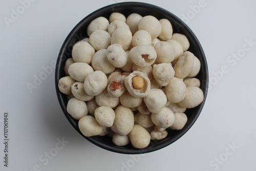 Kacang Atom, snack from Indonesia, made from peanut covered by flour dough then fried. On black bowl, isolated on white background, flat lay or top view photo