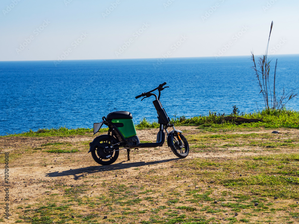 A black rental moped stands on the shore against the backdrop of the blue sea. Sunny weather.