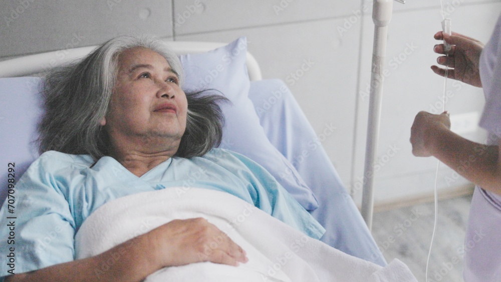 Obraz premium Asian nurse checks IV bag for elderly female patient in hospital room