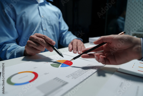 Group of business people meeting, discussion, brainstorming, pointing at graphs and charts to analyze market data, calculating balance sheets, accounts, net profits to plan company sales strategies. © crizzystudio