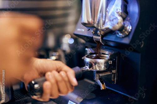 A barista holding a handle with a ground coffee pouring into a portafilter with a grinder. photo