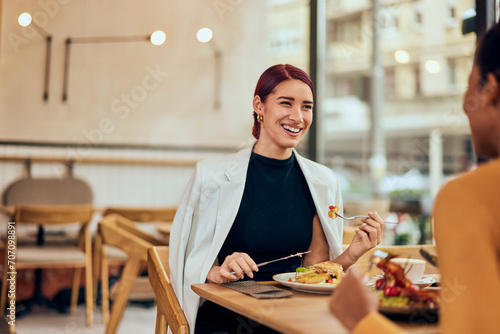 A smiling red-haired female  eating a breakfast with her African friend.