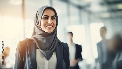 A young Middle-Eastern woman in a hijab smiling in an office setting. The concept of cultural diversity