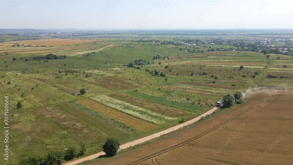 Aerial view of cargo truck driving on dirt road between agricultural wheat fields making lot of dust. Transportation of grain after being harvested by combine harvester during harvesting season Aerial view of cargo truck driving on dirt road between agricultural wheat fields making lot of dust. Transportation of grain after being harvested by combine harvester during harvesting season