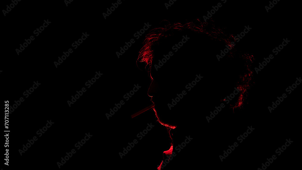 man with a cigarette in his mouth seen in profile in silhouette with red light illuminating his profile against black background man with a cigarette in his mouth seen in profile in silhouette with red light illuminating his profile against black background