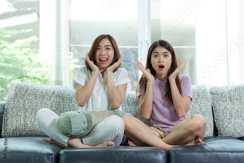 asian woman and friend sit at home on sofa bed watch tv movie.