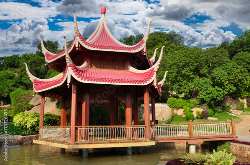 Traditional East Asian Pavilion with Curved Roof and Upturned Eaves Over Water, Surrounded by Lush Greenery