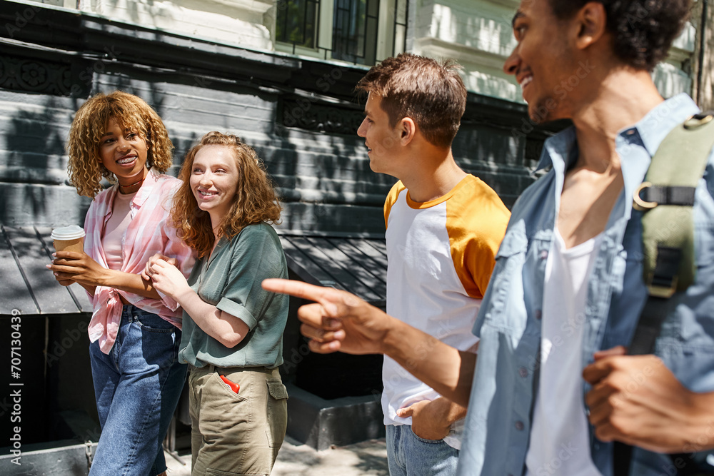 Obraz premium smiling african american man pointing with finger near stylish multiethnic friends on urban street