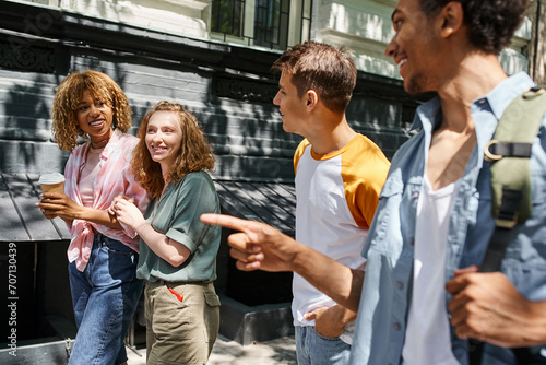 smiling african american man pointing with finger near stylish multiethnic friends on urban street