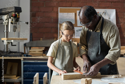 Waist up portrait of young girl measuring wood in workshop studio with senior carpenter helping © AnnaStills